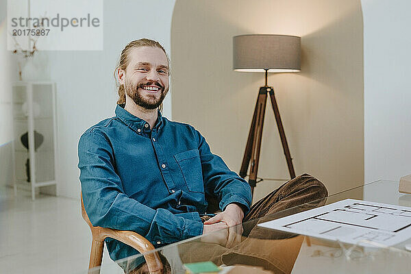 Glücklicher Innenarchitekt  der im Büro auf einem Stuhl sitzt