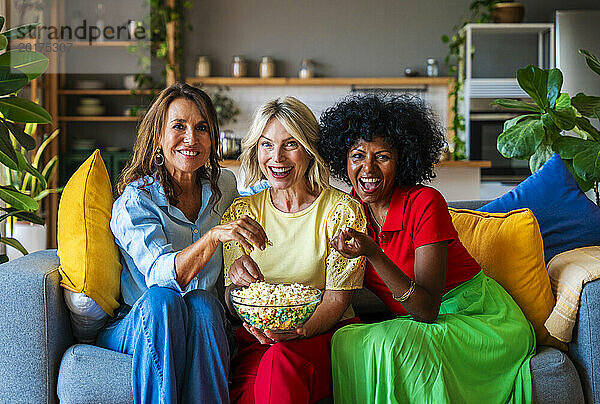 Fröhliche Freunde sitzen auf dem Sofa und teilen zu Hause Popcorn