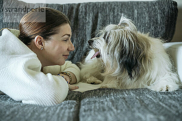Lächelnde Frau liegt Angesicht zu Angesicht mit Hund auf dem heimischen Sofa