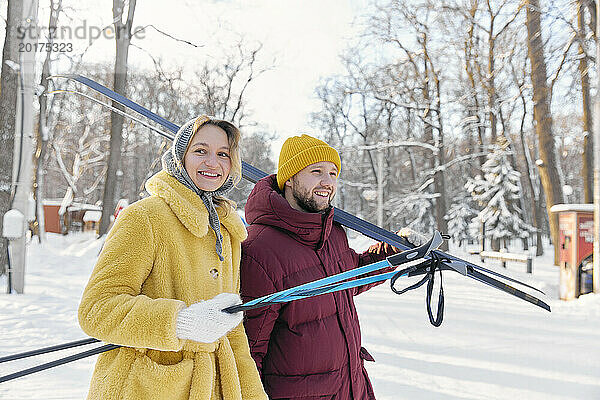 Glücklicher Mann und Frau mit Skiern im Winterwald