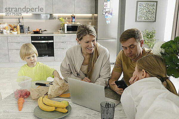 Father using smart phone with family having breakfast at dining table