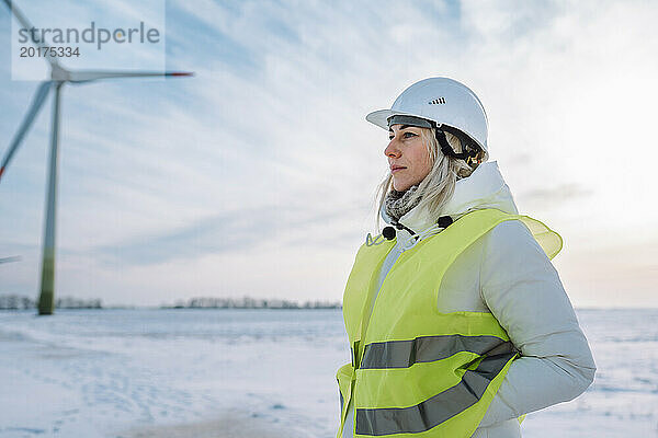 Ingenieur mit Händen in Taschen steht im Winter in der Nähe einer Windkraftanlage