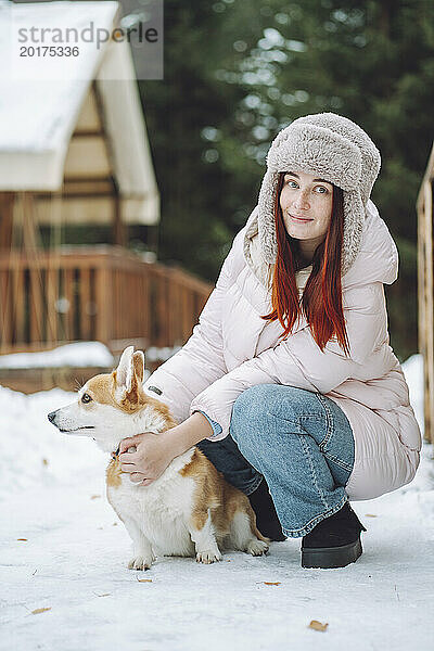 Frau trägt warme Kleidung und hält im Winter einen Corgi-Hund