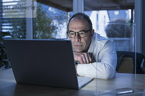 Freiberufler mit Brille und Videoanruf am Laptop im Heimbüro