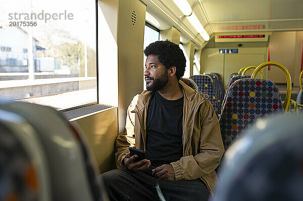 Mann hält Smartphone in der Hand und schaut aus dem Fenster in der U-Bahn