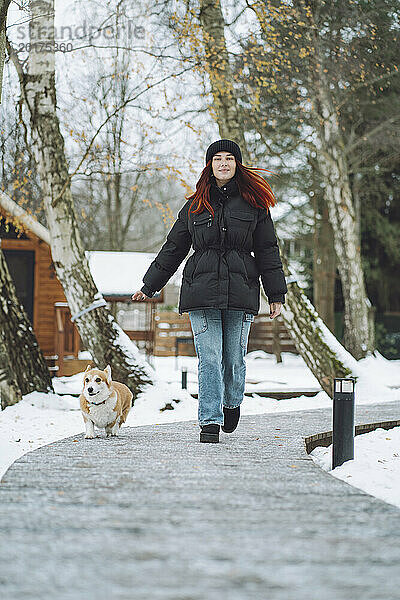 Junge Frau geht mit Corgi-Hund auf Fußweg spazieren