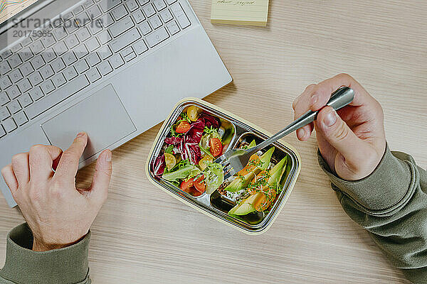 Freelancer working on laptop and having vegetarian food from lunch box