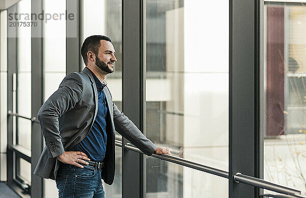 Lächelnder Geschäftsmann  der im Büro aus dem Fenster schaut