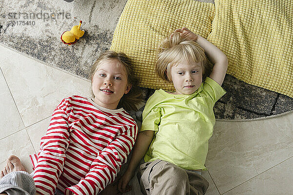Siblings lying on floor near pillow at home