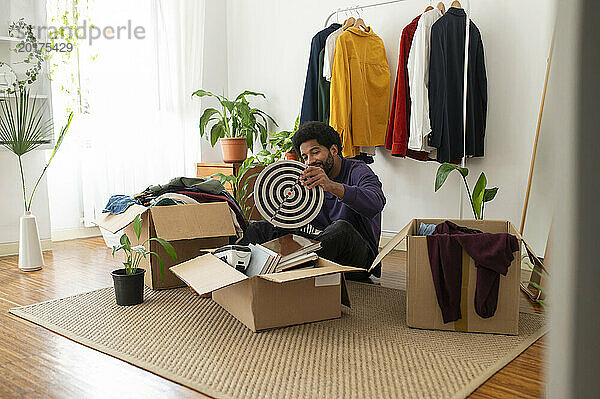 Junger Mann organisiert Kleidung und Gegenstände in Pappkartons