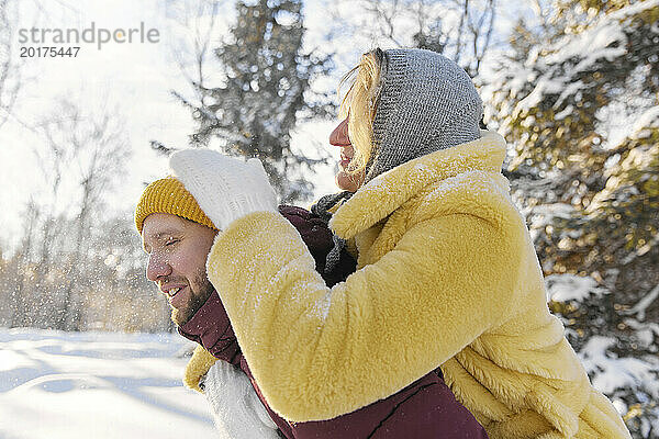 Junge Frau genießt Huckepackfahrt mit Mann im Winterwald