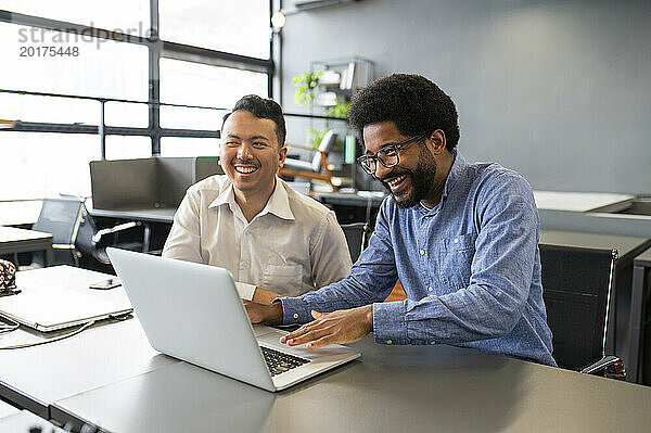 Glückliche Geschäftsleute diskutieren mit Laptop am Schreibtisch