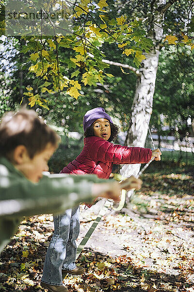 Mädchen stützt sich auf Seil  während sie mit Jungen im Park spielt