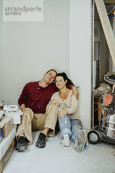 Glückliches Paar sitzt zusammen im Zimmer  während es das Haus renoviert