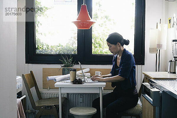Seitenansicht einer Architektin mit Laptop am Schreibtisch im Heimbüro