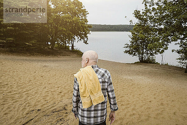 Rückansicht eines älteren Mannes mit Handtuch auf der Schulter  der in Richtung Fluss geht