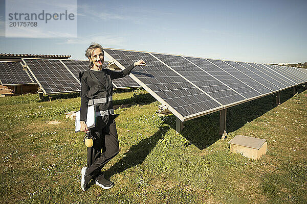 Porträt einer lächelnden leitenden Ingenieurin  die neben Sonnenkollektoren im Kraftwerk steht
