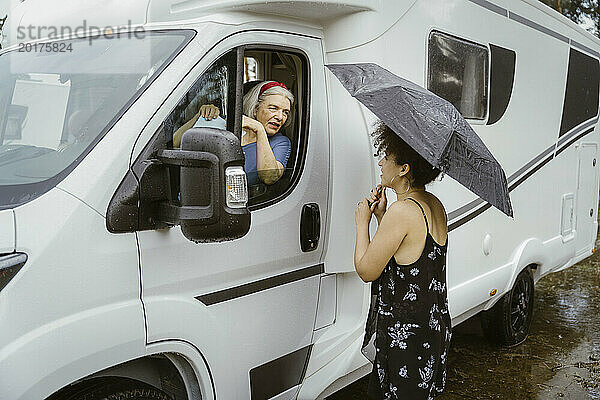 Ältere Frau sitzt im Wohnmobil und spricht mit junger Frau  die mit Regenschirm im Regen steht