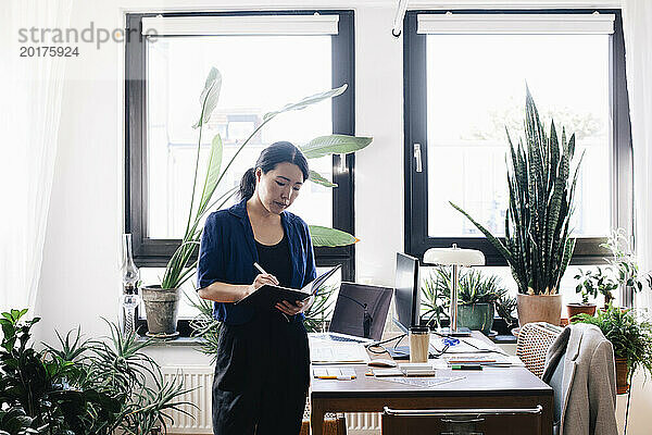 Selbstbewusste Architektin schreibt Tagebuch  während sie im Heimbüro am Schreibtisch steht