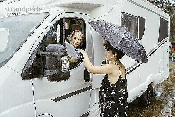 Junge Frau mit Regenschirm hilft Seniorin bei der Orientierung
