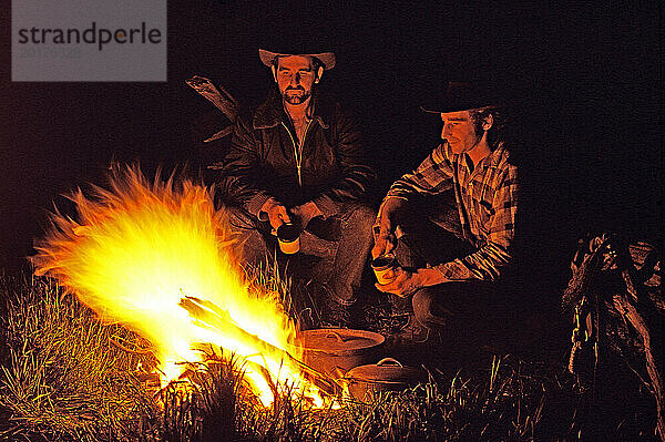 Junge Männer draußen am Lagerfeuer in der Nacht.