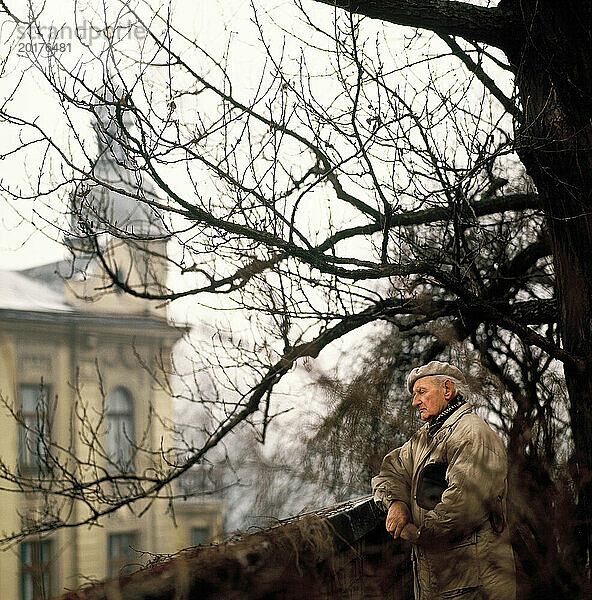 Polen. Provinz Kleinpolen. Alter Mann draußen mit Blick auf historisches Gebäude.