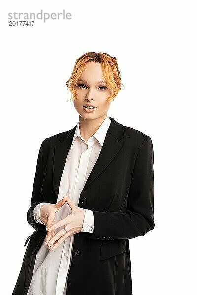 Selbstbewusste junge weibliche Führungskraft in einem formellen Anzug  die vor einem weißen Hintergrund steht  die Hände zusammenhält und in die Kamera schaut