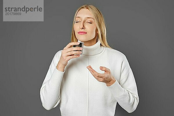 Eine junge Frau hält mit geschlossenen Augen eine Tasse mit frischem Kaffee in der Hand und atmet das Aroma ein