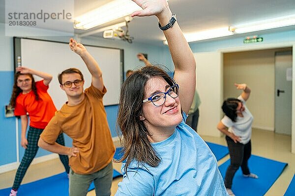 Glückliche Menschen mit besonderen Bedürfnissen  die in einem Fitnessstudio lächelnd trainieren und in die Kamera schauen  während sie den Rücken strecken