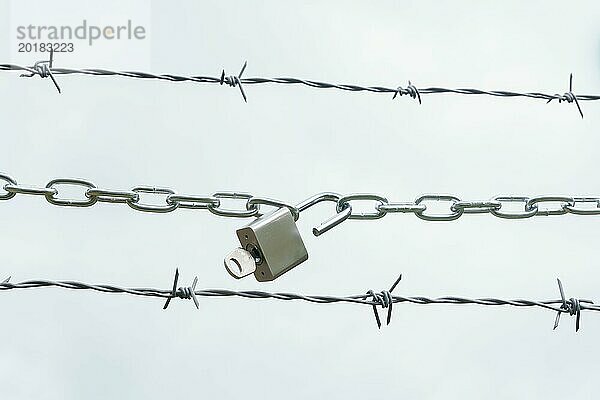 Kette mit offenem Vorhängeschloss auf einem Stacheldraht vor weißem Hintergrund  Freiheit Konzept