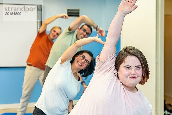 Fokus auf eine Frau mit Down Syndrom und eine Gruppe von Menschen mit besonderen Bedürfnissen  die sich in der Turnhalle dehnen