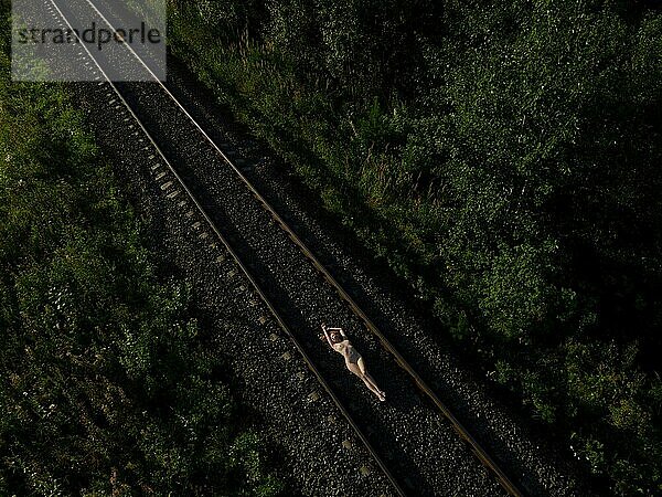 Draufsicht auf eine nackte Frau im Liegen auf einer Bahnstrecke bei Sonnenaufgang