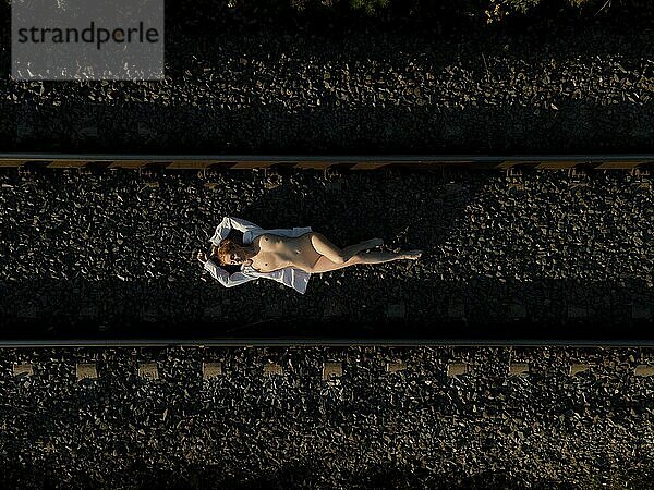 Draufsicht auf eine nackte Frau im Liegen auf einer Bahnstrecke an einem sonnigen Tag