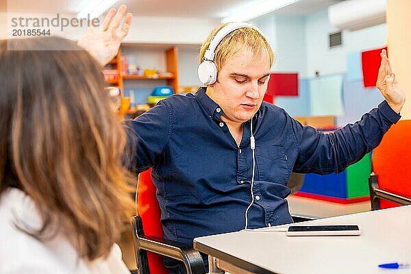 Mann mit geistiger Behinderung  der neben einem Freund in einer Tagesstätte über Kopfhörer Musik hört