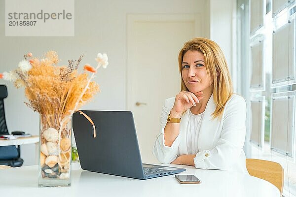 Horizontales Foto mit Kopierbereich eines weiblichen Immobilienmaklers  der in die Kamera lächelt und im Büro vor einem Computer sitzt