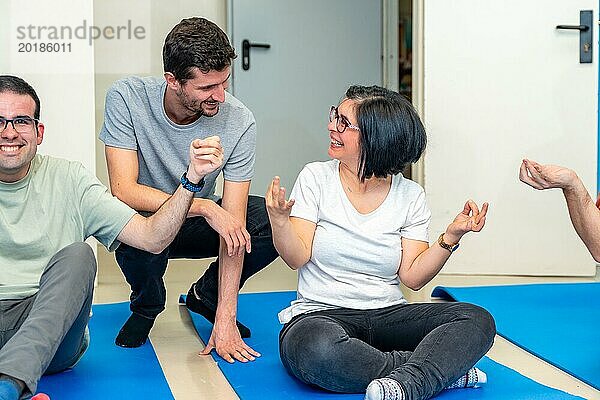 Yogalehrer im Gespräch mit einer glücklichen erwachsenen behinderten Frau  die während einer Yogastunde auf einer Matte sitzt