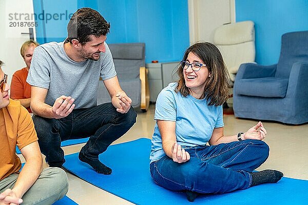 Yogalehrer  der einer behinderten Frau  die auf einer Matte sitzt  in einer Yogagruppe den Lotussitz beibringt