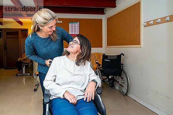 Betreuerin schiebt den Rollstuhl einer behinderten Frau in einer Tagesstätte für Menschen mit besonderen Bedürfnissen