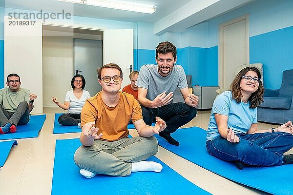 Freundlicher männlicher Yogalehrer  der eine Klasse mit Menschen mit besonderen Bedürfnissen und Down Syndrom leitet