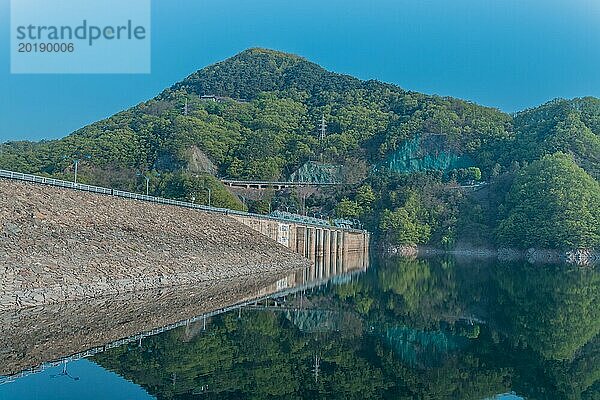 Schönes Seegebiet mit Damm und Baumgrenze  die sich im ruhigen blauen Wasser des Daecheon Sees in Südkorea spiegeln
