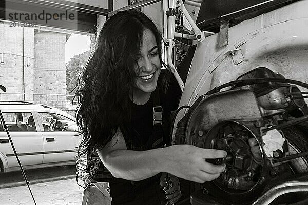 Eine fröhliche weibliche Mechanikerin arbeitet an einem Moped italienischer Vintage Roller Motorradmotor in einer Werkstatt  echte Frauen  die traditionelle Männerarbeiten der Vergangenheit ausführen  Schwarz Weiß Foto