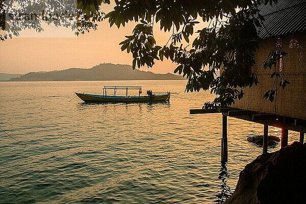 Ein einsames Boot gleitet auf dem ruhigen Wasser unter einem Sonnenuntergangshimmel in der Nähe einer Baumsilhouette. Insel Koh Sdach  Kambodscha  Asien