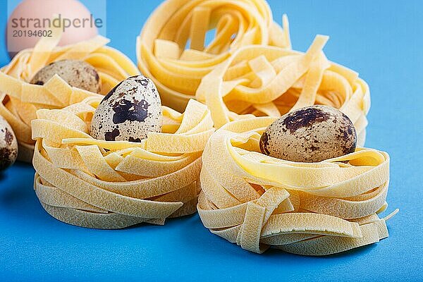 Rohe  ungekochte Tagliatelle Nudeln mit Wachteleiern auf blauem  pastellfarbenem Hintergrund. Seitenansicht  Nahaufnahme