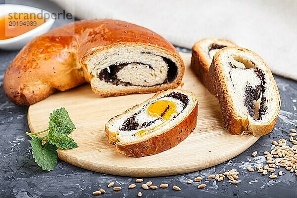 Hausgemachte Hefebrötchen mit Mohn und Honig auf einem hölzernen Küchenbrett auf einem schwarzen Betonhintergrund. Seitenansicht. Nahaufnahme  selektiver Fokus