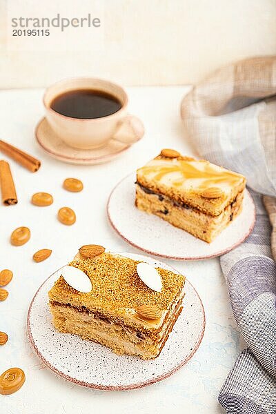 Honigkuchen mit Milchcreme  Karamell  Mandeln und einer Tasse Kaffee auf einem weißen Betonhintergrund und Leinenstoff. Seitenansicht  selektiver Fokus  Nahaufnahme