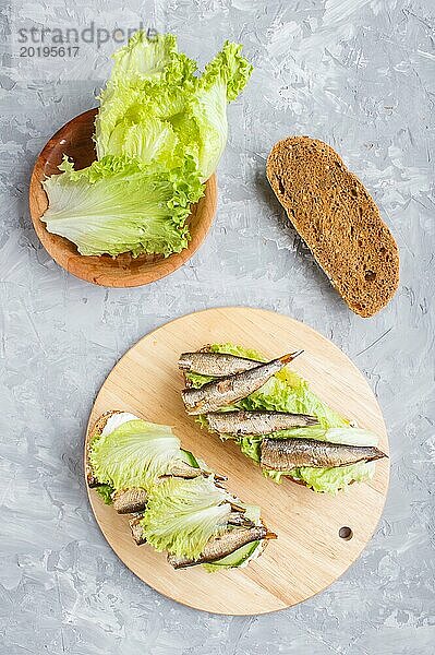 Sprotten Sandwiches mit Salat und Frischkäse auf Holzbrett auf grauem Beton Hintergrund. Ansicht von oben  flach legen