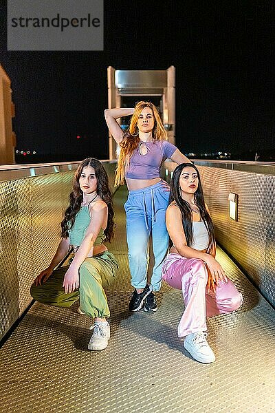 Vertikales Porträt einer Gruppe von drei schönen jungen Breakdancern  die nachts auf einer Brücke zusammen posieren