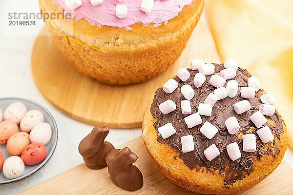 Hausgemachte glasierte und dekorierte Osterkuchen mit Schokoladeneiern und Kaninchen auf weißem Betonhintergrund und gelbem Textil. Seitenansicht  Nahaufnahme  selektiver Fokus