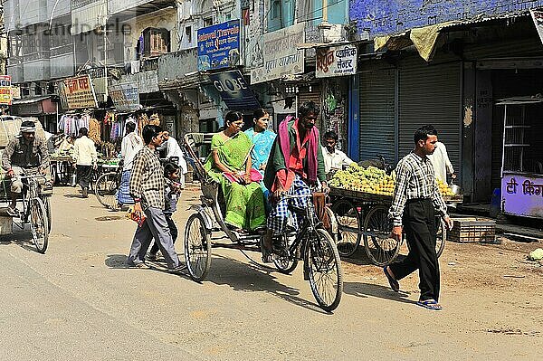 Personen in traditioneller Kleidung fahren auf Fahrradrikschas durch eine Stadtstraße  Varanasi  Uttar Pradesh  Indien  Asien