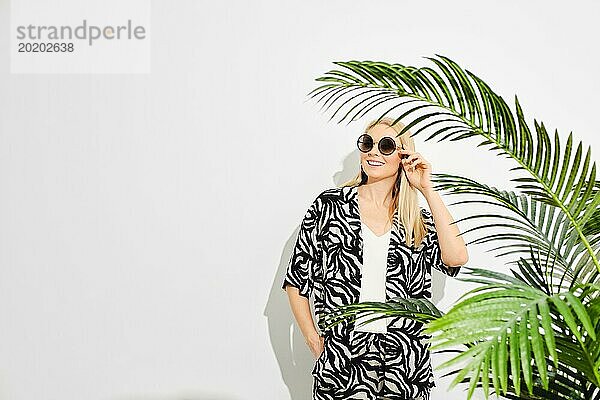 Eine glückliche Frau steht zwischen leuchtend grünen Palmenblättern  die ein Gefühl von Geheimnis und Verbundenheit mit der Natur vermitteln. Sie trägt ein Outfit mit Zebramuster  das die Mode mit der natürlichen Welt verbindet